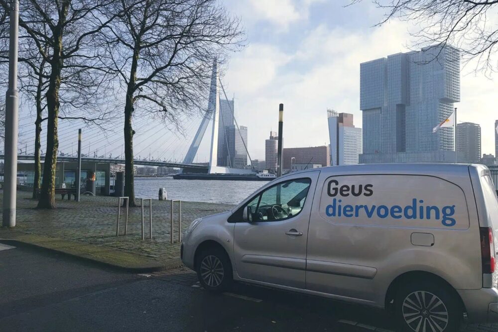 Bestelbus van Geus Diervoeding aan de Maas, met de Erasmusbrug en de Rotterdamse skyline op de achtergrond